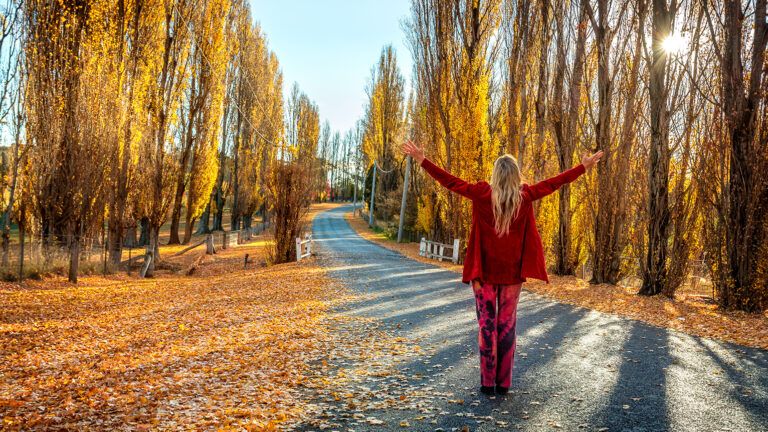 A woman raises her arms in gratitude on a country road in autumn