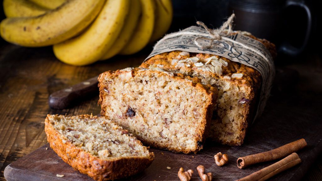 Sliced banana bread loaf with walnuts and cinnamon on wooden board.