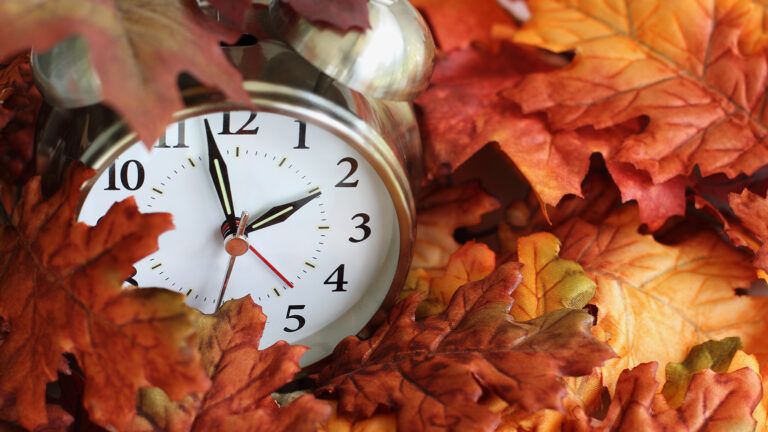 A clock showing one minute till 2 rests in a pile of leaves