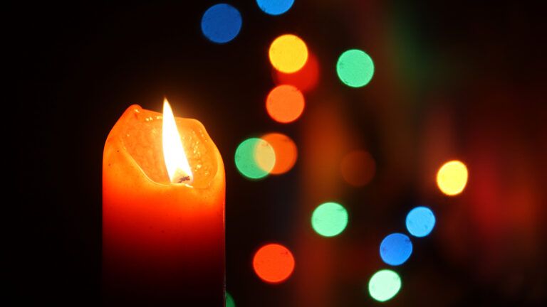 A Christmas candle with colorful lights in the background