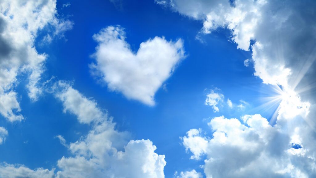 Heart shaped cloud over cloudy and sunny sky with sunbeam