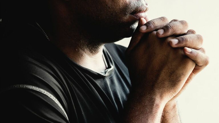 A man's hands are clasped in prayer