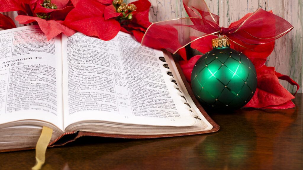 A green Christmas ornament next to an open Bible displaying a Christmas verse about peace
