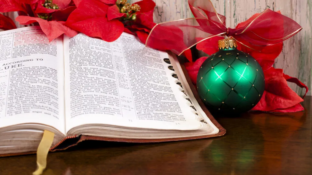 A green Christmas ornament next to an open Bible displaying a Christmas verse about peace