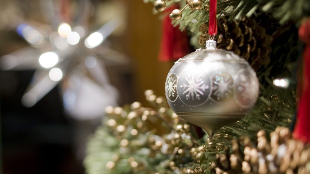 Close up of a silver Christmas ornament hanging on a branch of a Christmas tree.