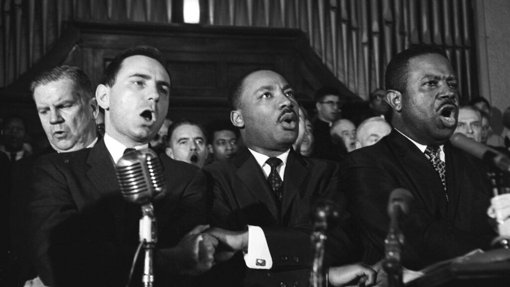 Martin Luther King Jr., Ralph Abernathy (right) unidentified men sing in Selma, Alabama church.