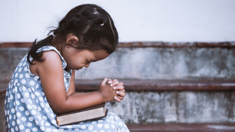 A little girl bows her head in prayer
