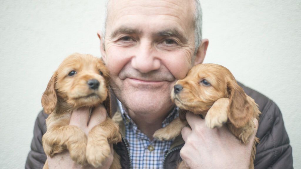 A senior citizen holding two puppies.