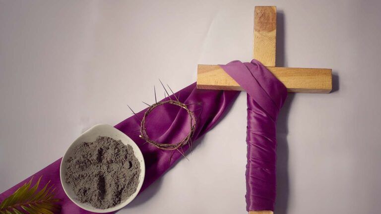A wooden cross wrapped in purple ribbon with lent symbols like ashes and palm to show an ash wednesday reflection