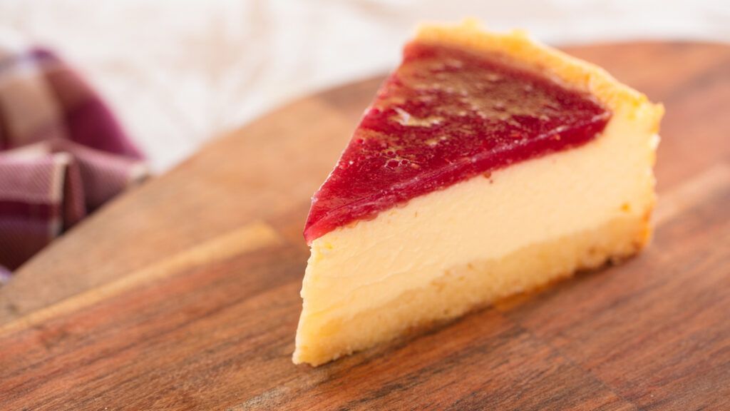 A slice of strawberry cheesecake on a wooden platter.