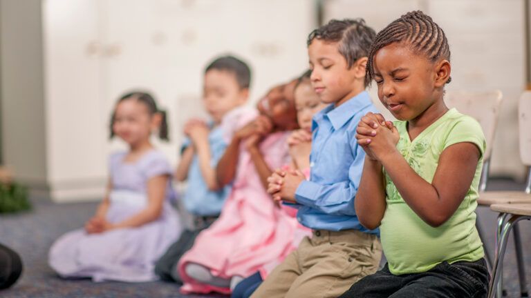 A group of young children kneel, hands clasped in prayer