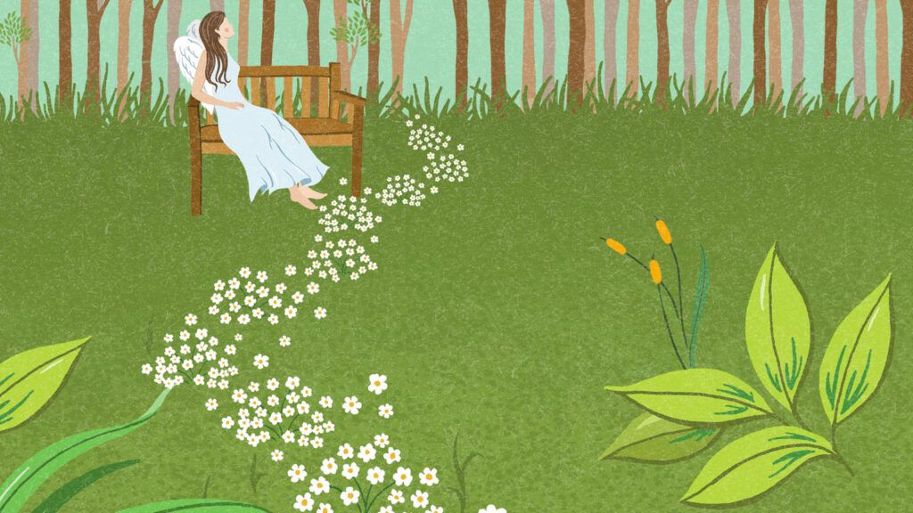 A trail of small, white flowers lead to an angel sitting on a bench in a garden.