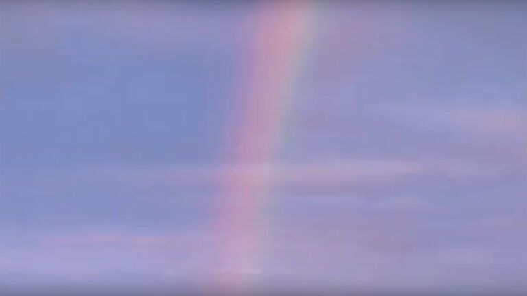 A rainbow arcs across a blue sky