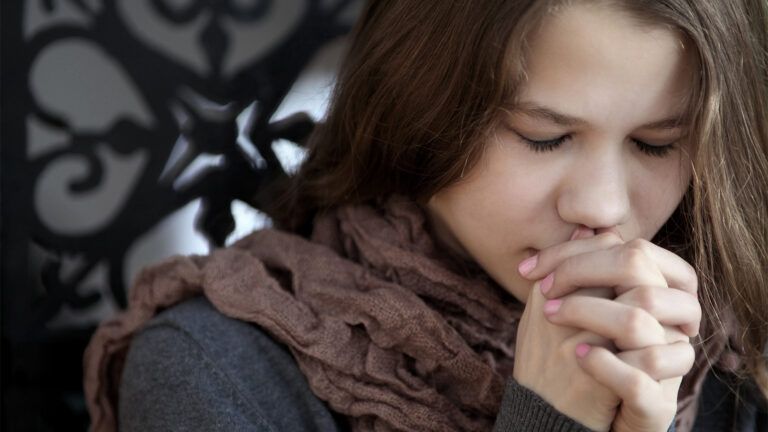 A young woman clasps her hands in prayer