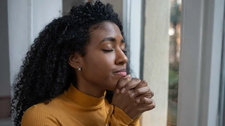 Woman in yellow saying her spring prayers in front of a window