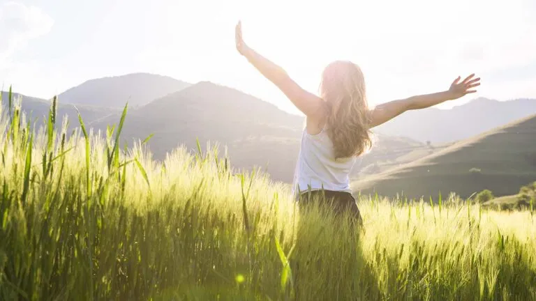 Woman with her arms raised saying her spring prayers in the middle of a field