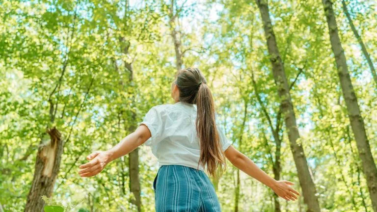 Woman with her arms raised saying her spring prayers in the woods