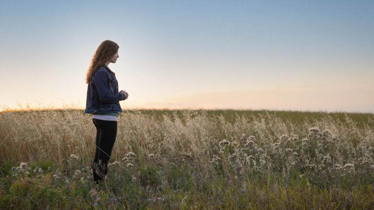 Young woman standing in a field saying her spring prayers