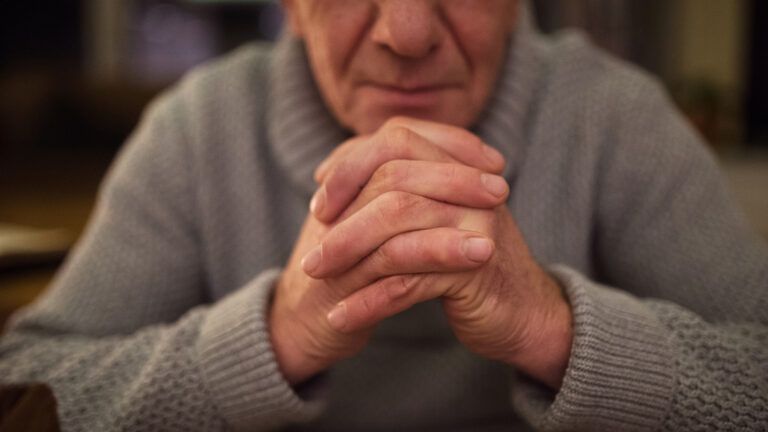 A senior man clasps his hands in prayer