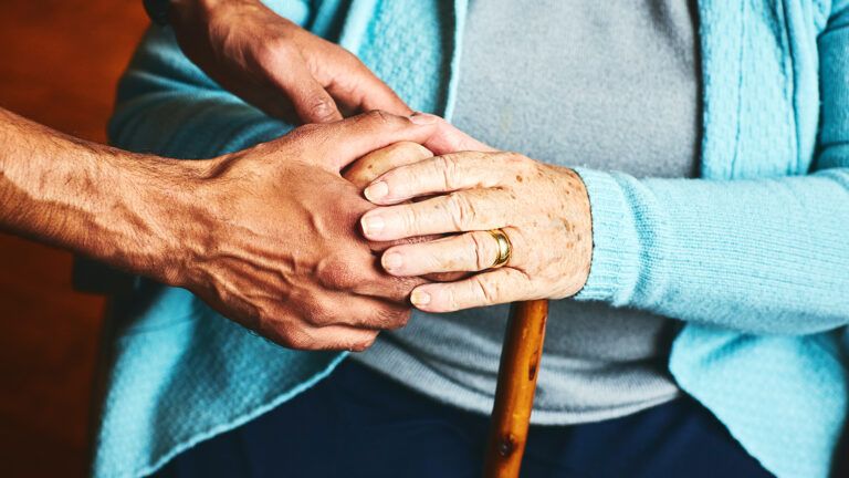 A caregiver's hands clasp the hands of his loved one