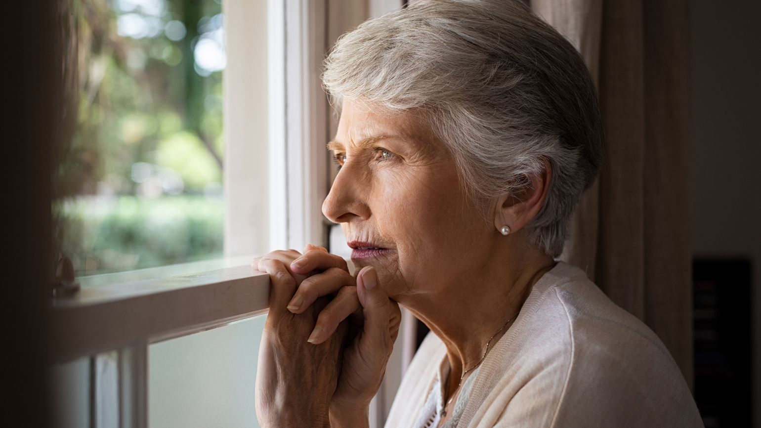 A senior woman looking contemplative out of a window.