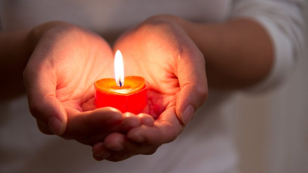 A woman's hands holding a a lit red candle.