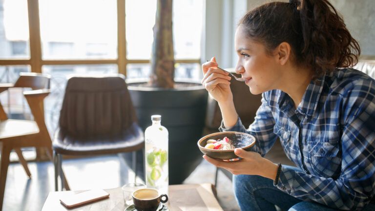 A woman eats a healthy breakfast in her home as sunlight pours in.
