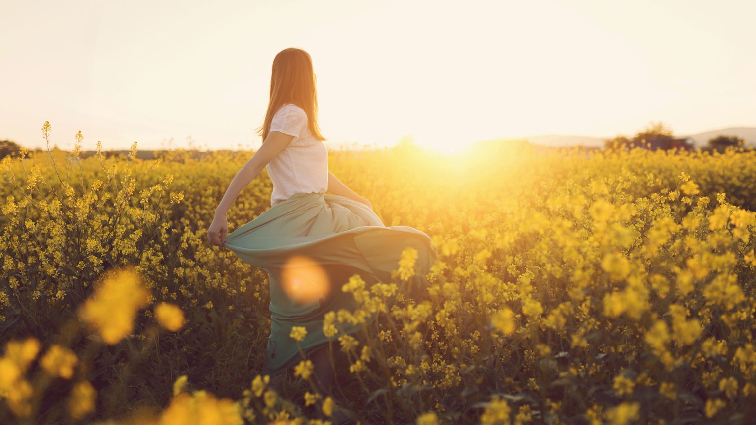 A woman dancing through a field of yellow flowers.