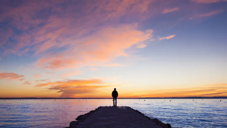 A silhouette of a man in contemplation on a jetty as the sun sets.