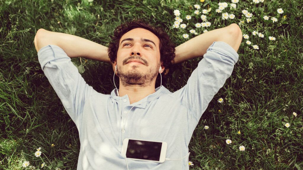 A man relaxing on the grass while listening to music.