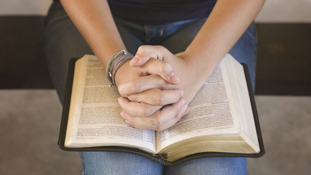 A teenage girl praying with the Bible open.