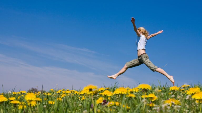 A woman joyfully leaps in a field of flowers
