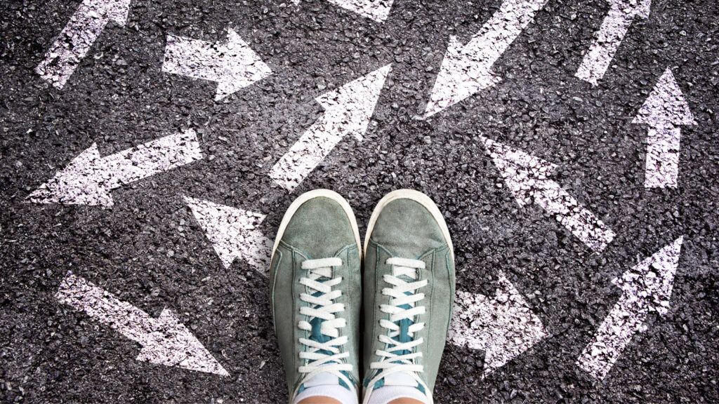 Sneaker shoes and arrows pointing in different directions on asphalt ground.