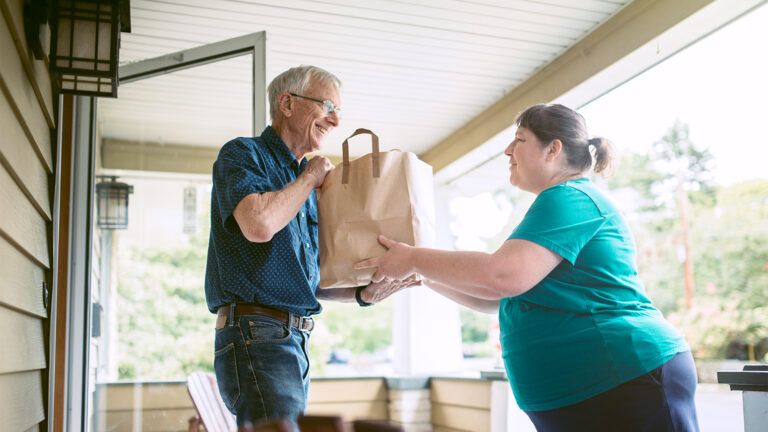 A woman gives groceries to a senior neighbor