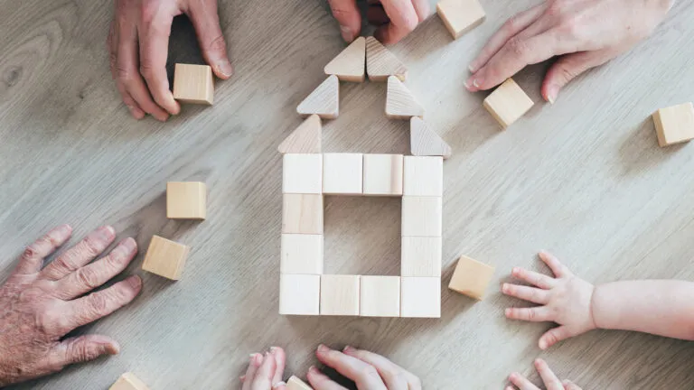 Family members using wooden blocks to form a house.