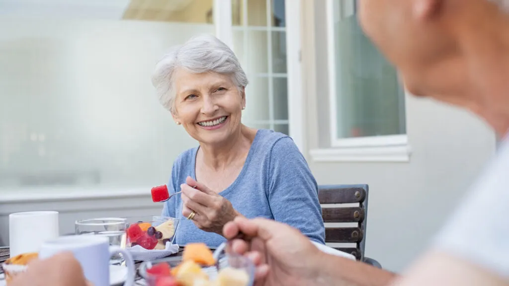 A woman eating a healthy bowl of fruit with a companion.