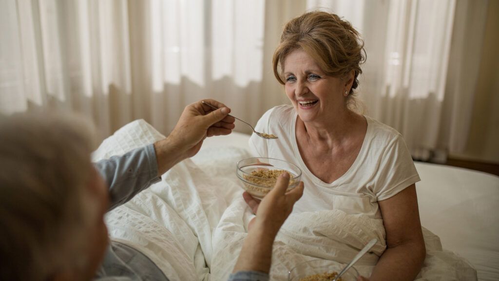 A woman being fed oatmeal in her bed.