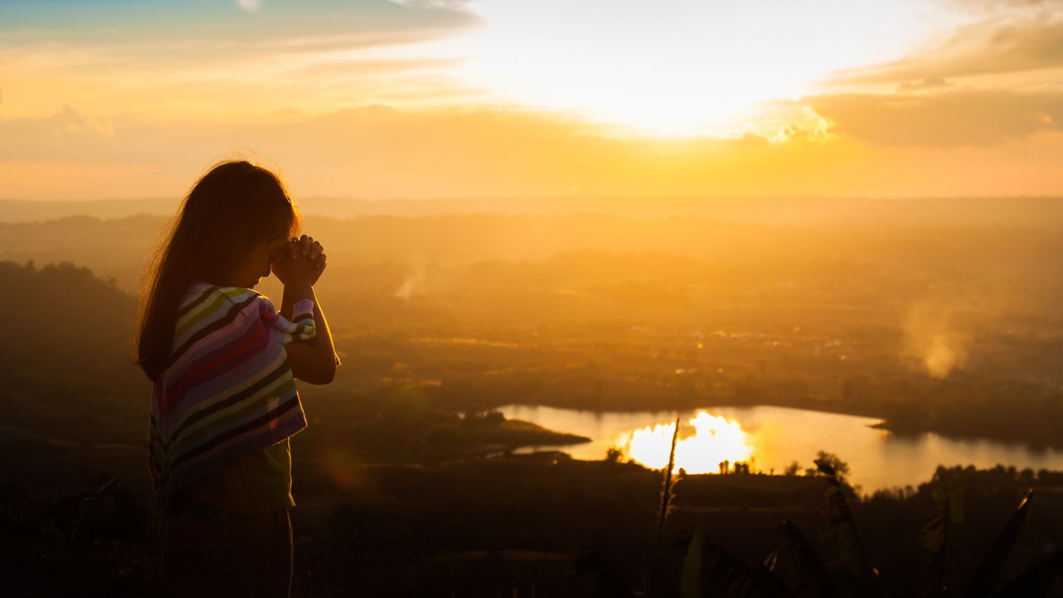 A young girl praying outdoors during a brilliant sunset.