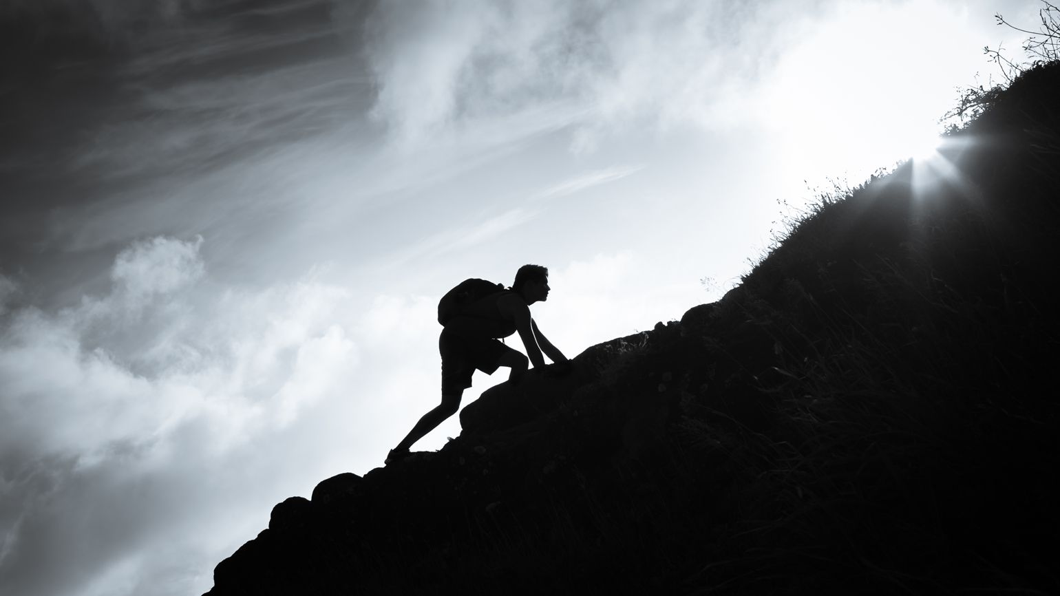 A silhouette of a person climbing up a large mountain.