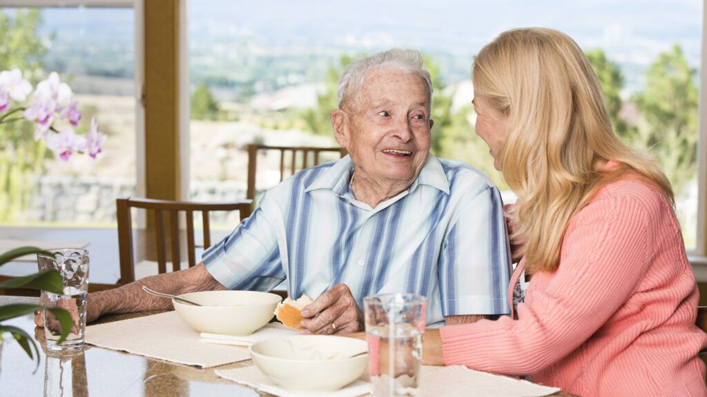 An older gentleman's daughter helps him eat soup at the table.