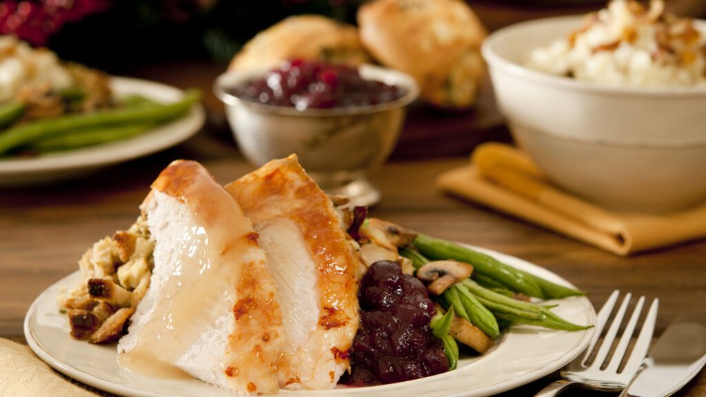 A dinner plate with roasted turkey, string beans, cranberry sauce and stuffing.