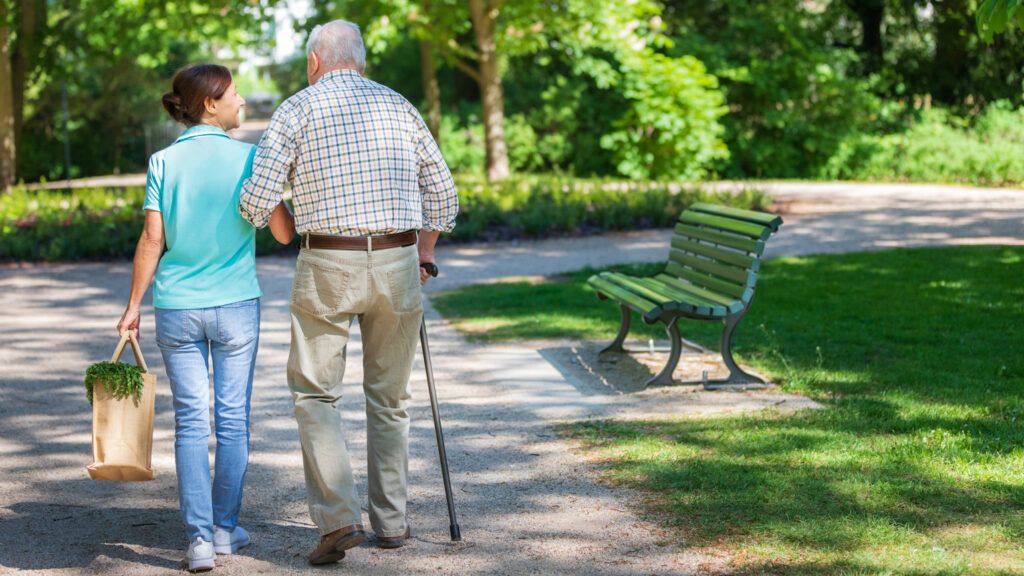 A caregiver woman with a senior man walking in the park.