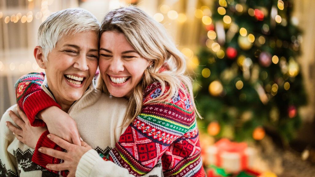 Two women hug in front of Christmas tree