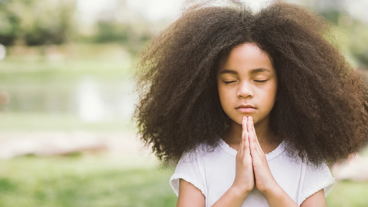 A young girl praying outdoors.