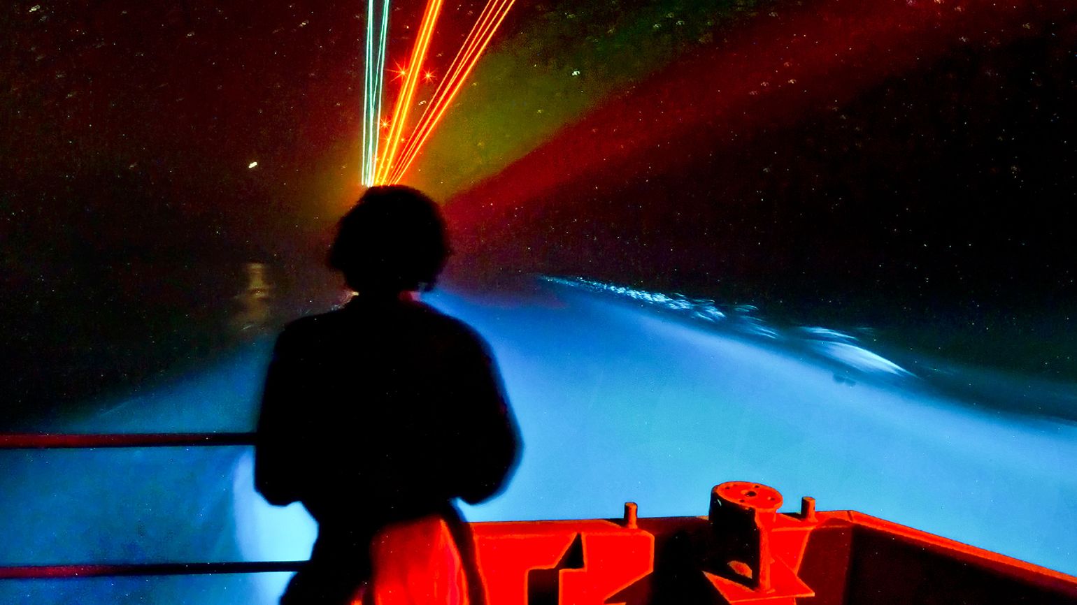 A sailor aboard the USS Carl Vinson watches a trail of bioluminescent organisms the carrier leaves in its wake.