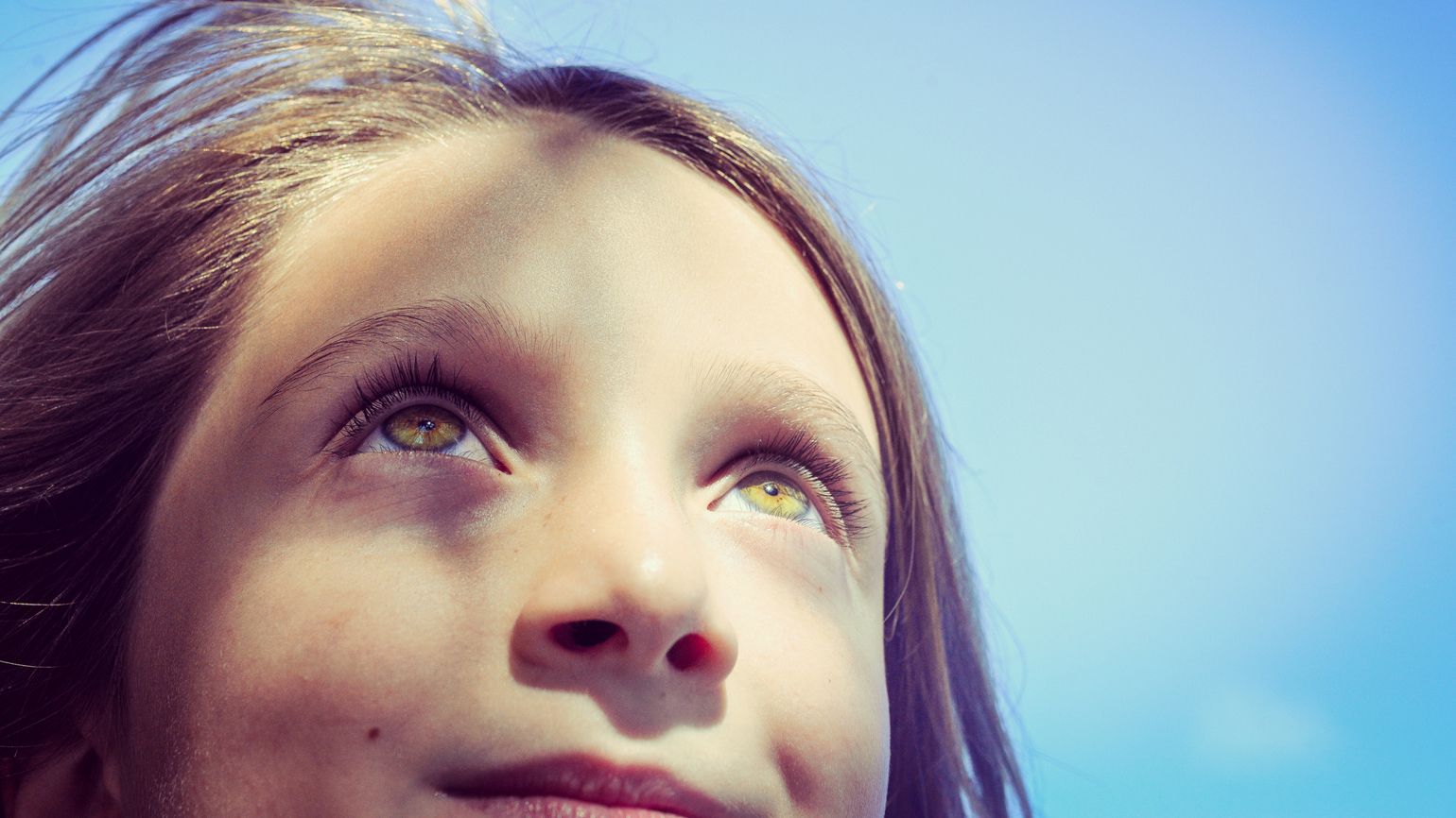 A close up of a young girl looking up at the sky.