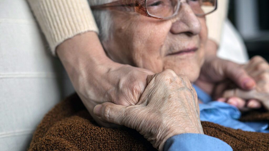 A family member clasps hands with loved one with dementia