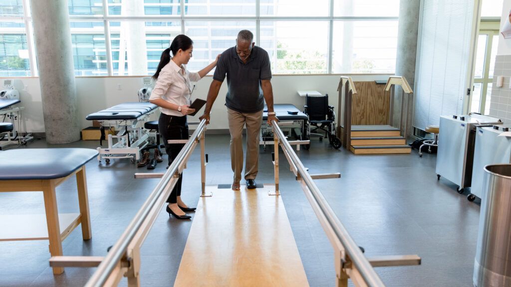 An older man undergoes walking physical therapy with guidance.