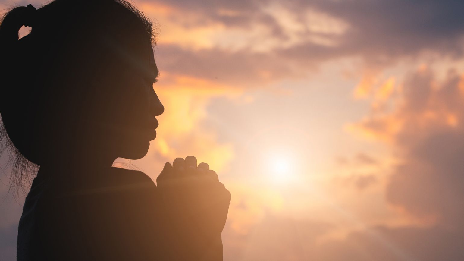 Silouette of a young woman in prayer.