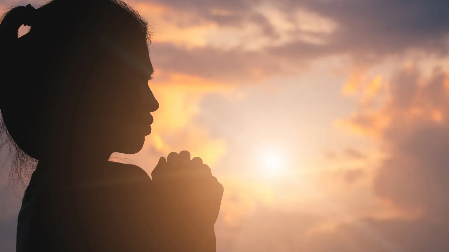 Silouette of a young woman in prayer.